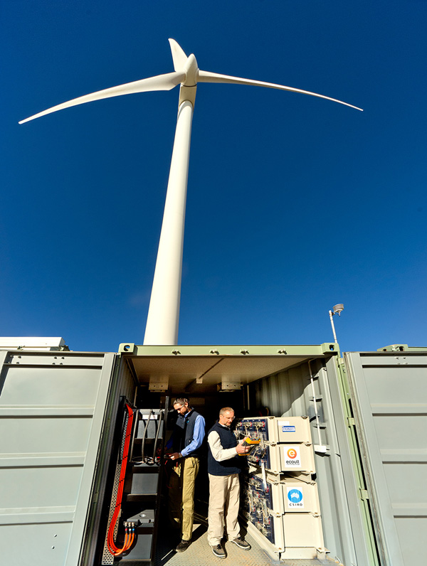 Two researchers in a battery bank underneath a wind turbine.