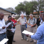 Local Africans and foreign scientists stand in a carpark reading pieces of paper