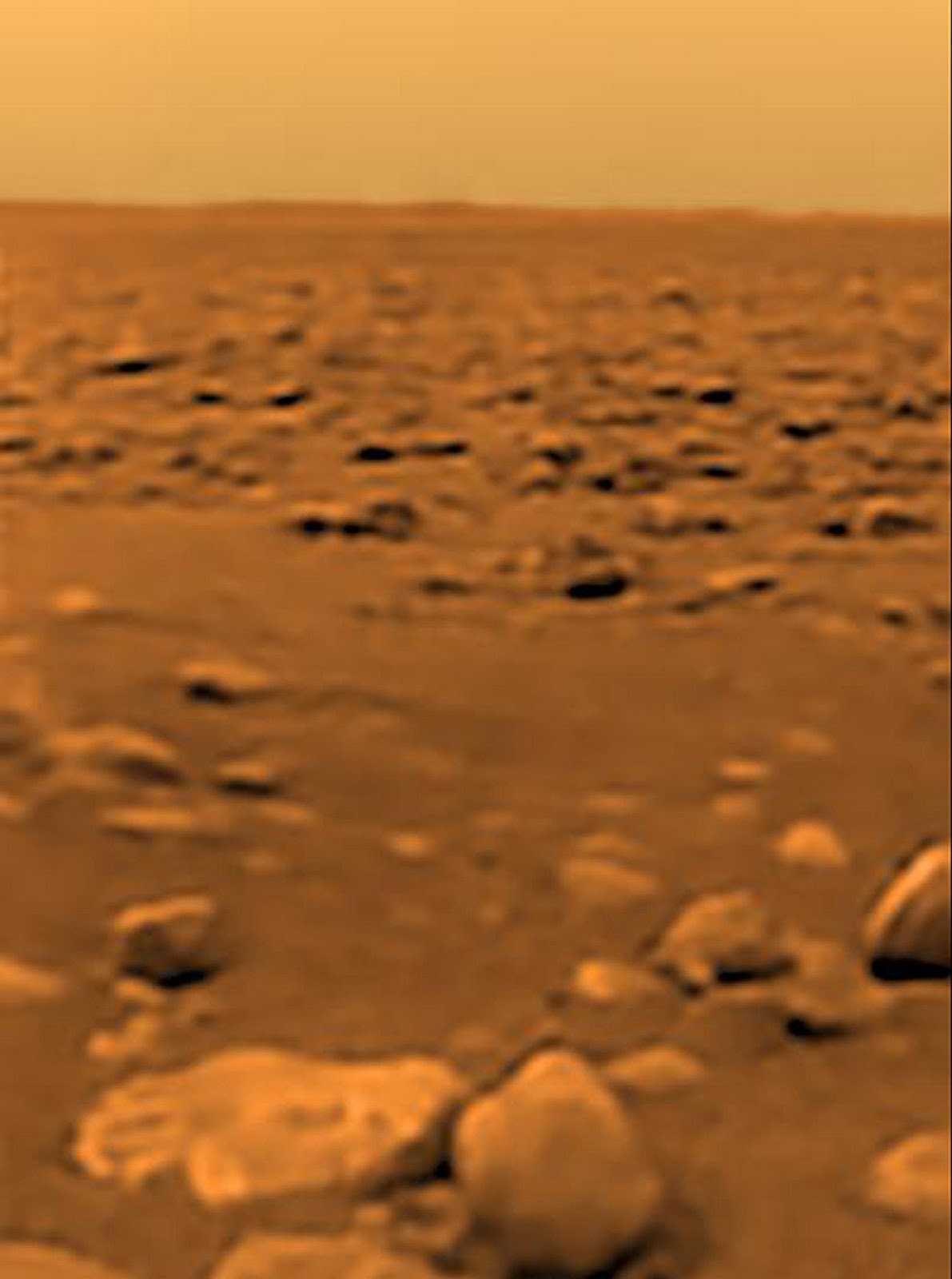 The surface of Titan, a moon of Saturn, showing rocks on flat ground.