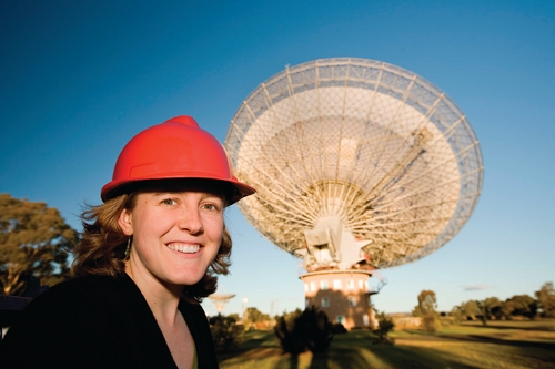 Naomi McClure-Griffiths in front of the Parkes radio telescope, wearing a hard hat.