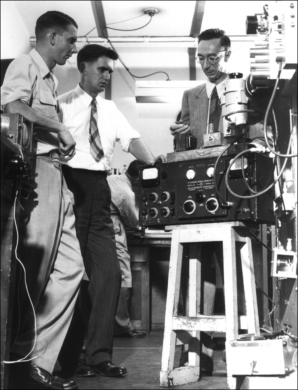 Three engineers in a 1940s laboratory looking at radio equipment.