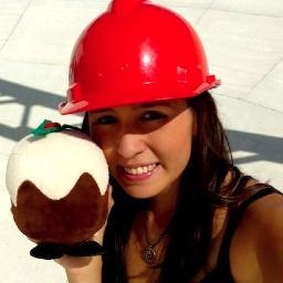 A woman in a red hard hat, holding a fake Christmas pudding.
