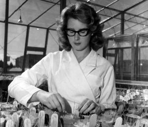 A woman in a lab coat working with plants in a glasshouse