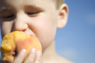 Boy biting into peach with blue sky in the background
