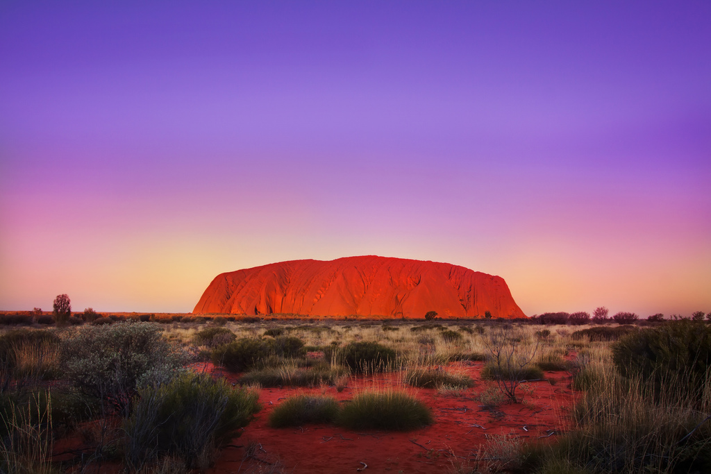 Uluru, a monolithic rock in central Australia, glowing orange at sunset.