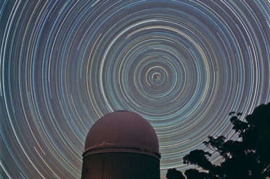 Star trails - bright concentric circles in the night sky - with a dome-shaped building in the foreground.