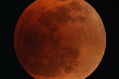 The full Moon, rusty red in colour, and dark sky
