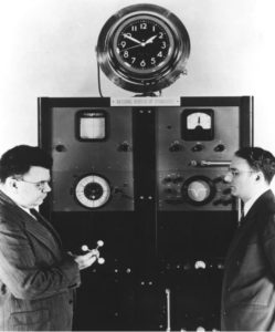 Two US Government officials stand in front of thefirst official atomic clock. 