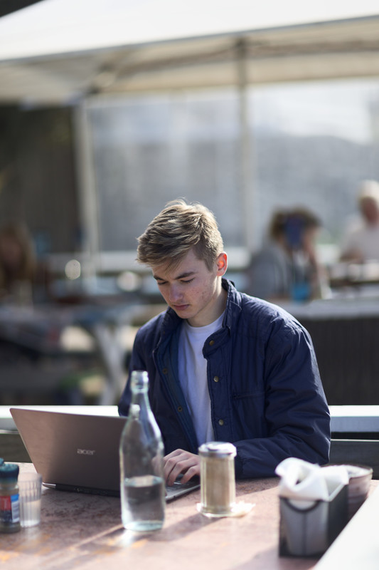 Teenage male seated in cafe using laptop computer.
