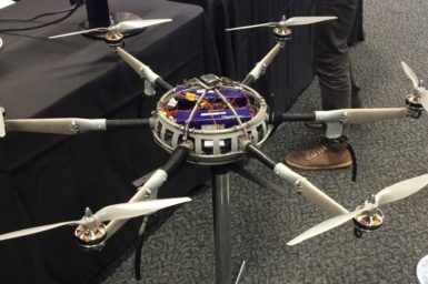A spherical drone with six arms and propellers sits on a stand at an exhibition