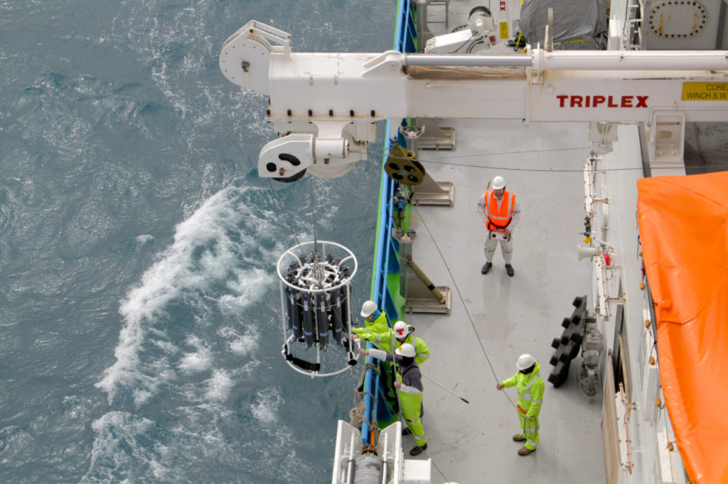 Sampling equipment being lowered into ocean from crane on ship