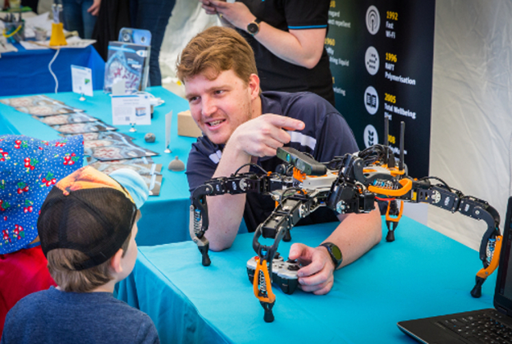 A researcher showing a six-legged robot to a small child at National Science Week