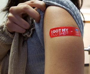 A sleeve lifted up to exposure a shoulder displaying an "I got my fly shot" plaster.