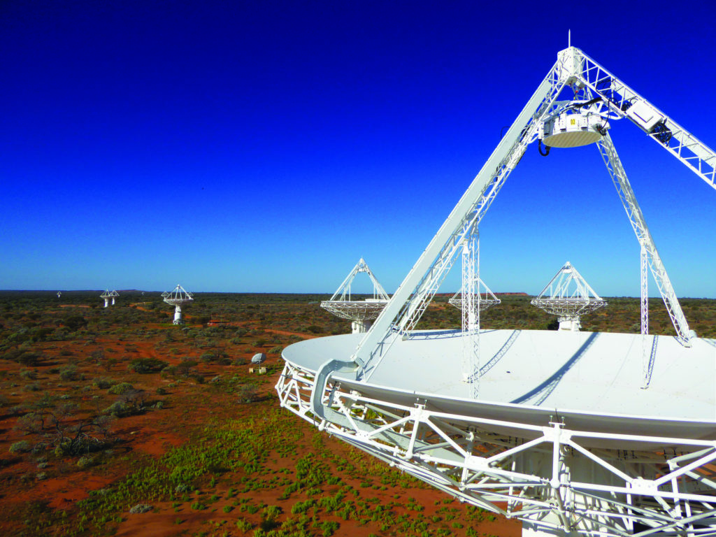Several white radio telescopes scattered across a dry red flat landscape of western Australia.