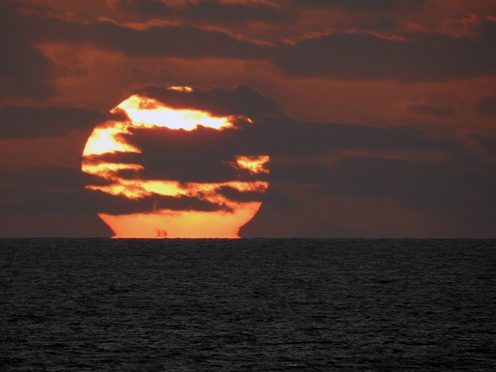 Sun is setting over the ocean with clouds covering it from view