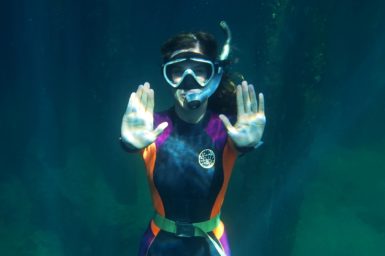 Anna cresswell underwater in scuba gear pushing an imaginary button