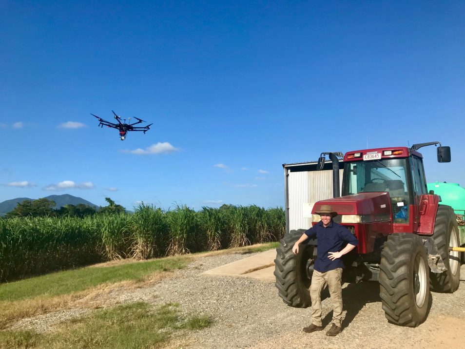 A man and a tractor beside a sugar cane field with a drone