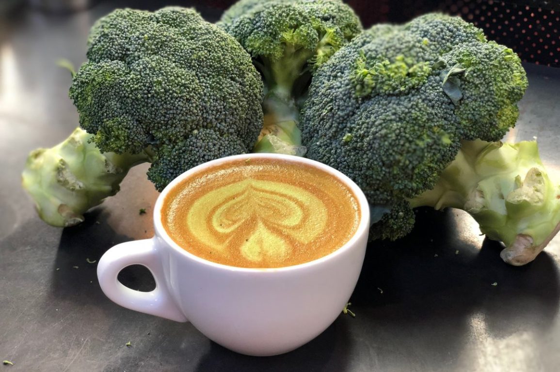 A broccoli latte surrounded by bunches of raw broccoli