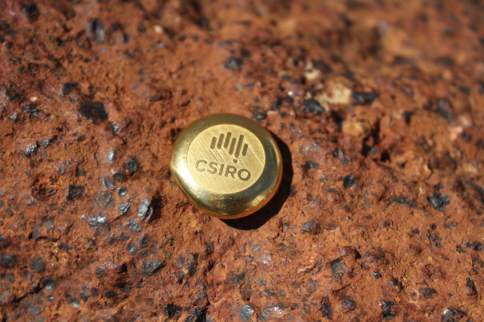 round gold ingot featuring CSIRO logo resting on a slice of rock ore