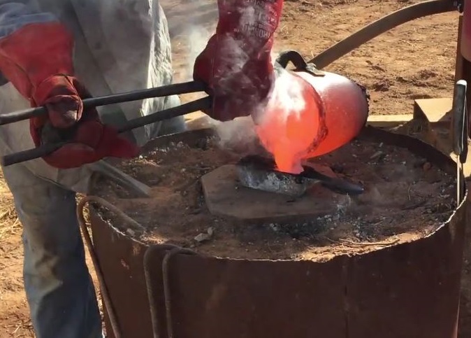 Red-hot crucible of gold being poured into a rectangular metal bar mold