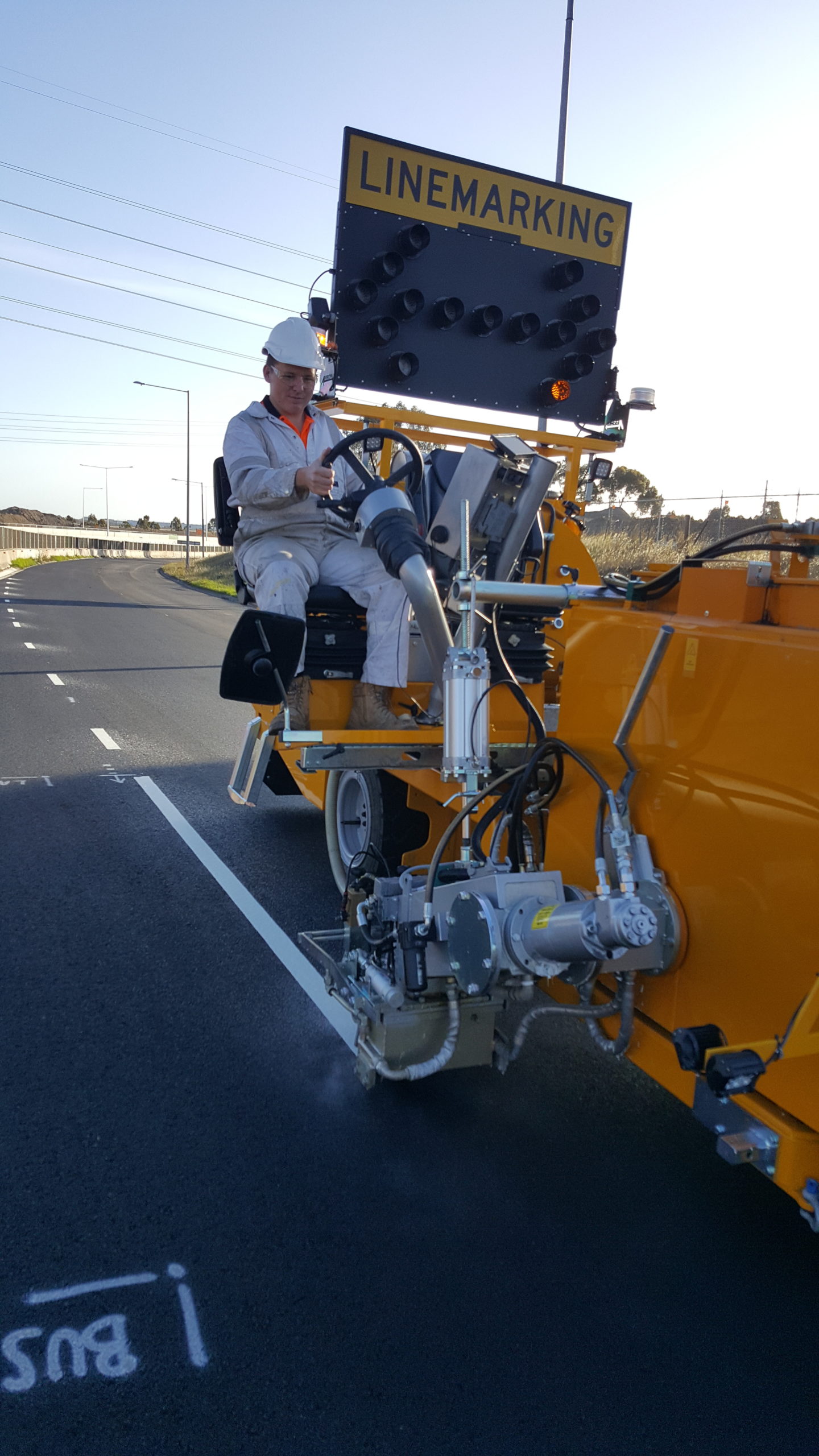 Person driving a line marking vehicle as it sprays white paint lines onto the road