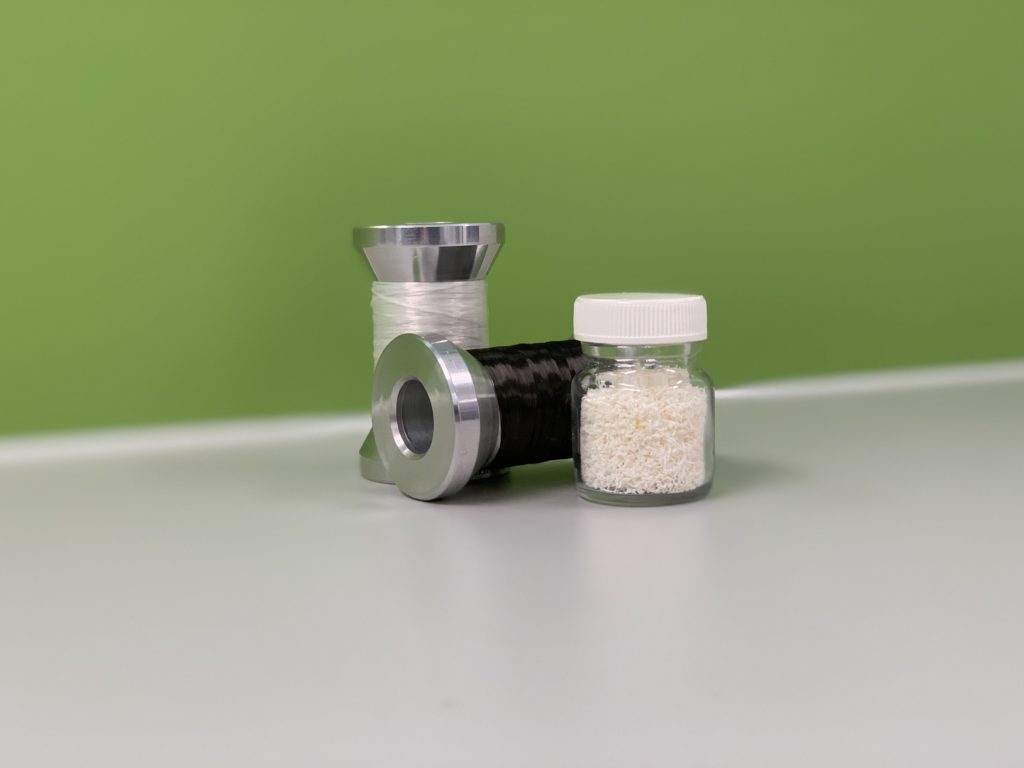 a jar of white polymers and two reels one with white and one with black fibre wrapped around them