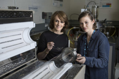 Chief scientist Cathy Foley smiling, standing next to a female student in a dark blue shirt, both looking at GraphAir lab technology