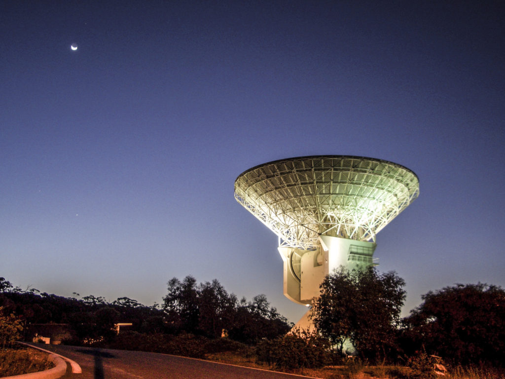 White dish-shaped antenna with the night sky behind it.