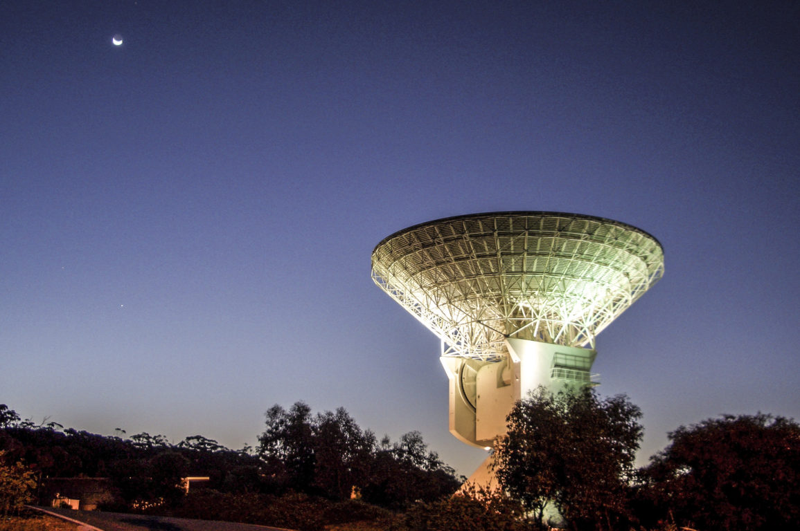 White dish-shaped antenna with the night sky behind it.