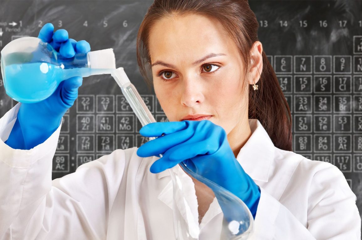 female chemist pouring chemicals with a blackboard showing the periodic table in the background