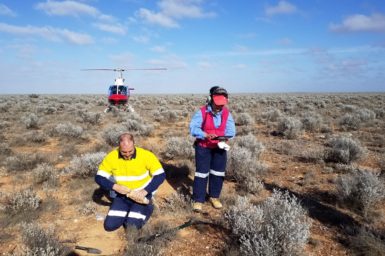 Male and female scientists taking soil samples from a remote landscape showing a helicopter in the background