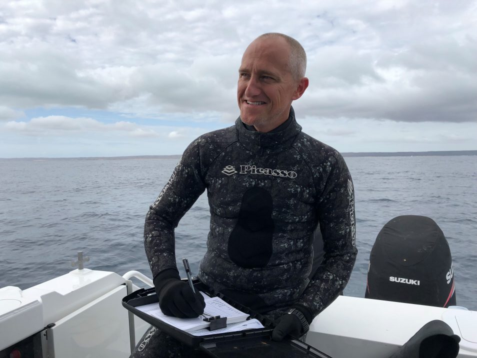 Dr Richard Pillans wears a wetsuit while sitting on a boat