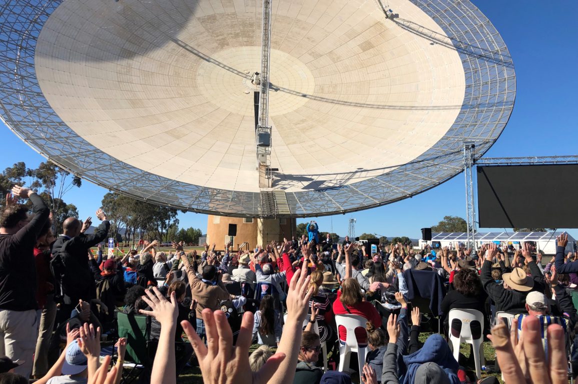 Crowd of people raising hands in front of the Dish