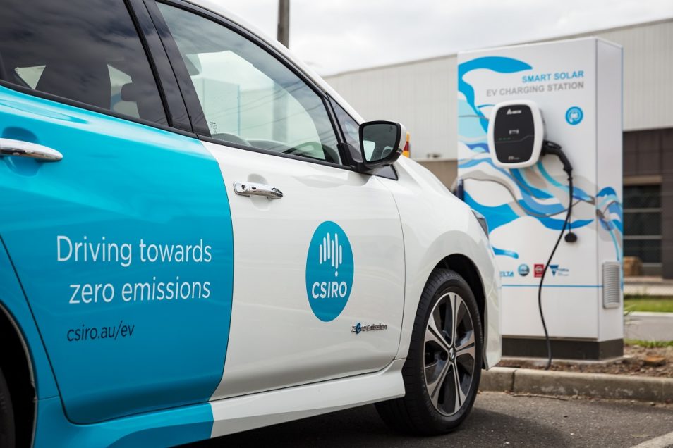 a car facing away from the camera. The door closest to the camera has text which reads "Driving towards zero emissions; csiro.au/ev" There is a smart charging station in the background. 