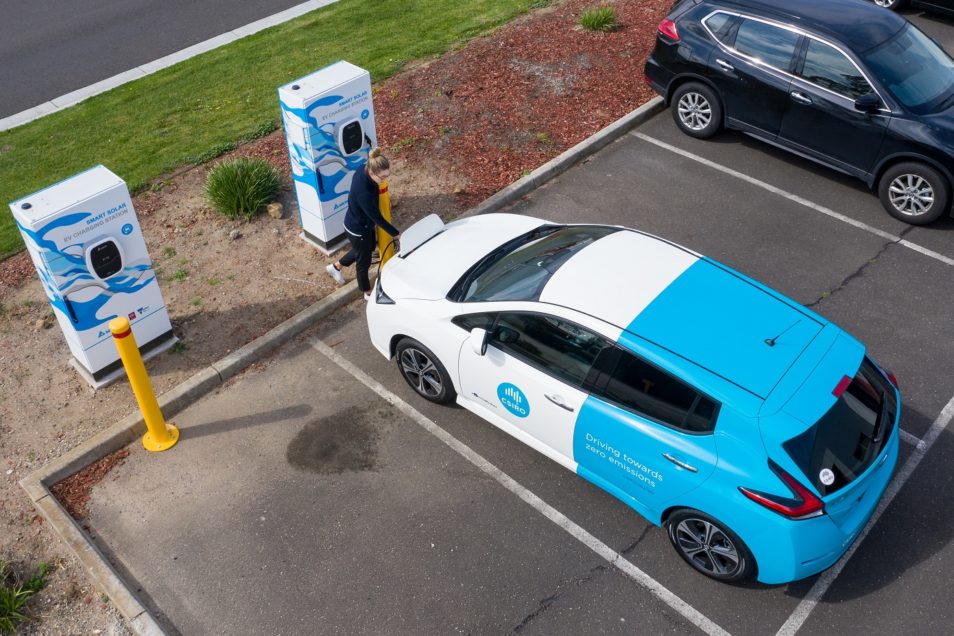 An aerial shot of a woman charging the electric vehicle like you would filling up petrol in the car. 