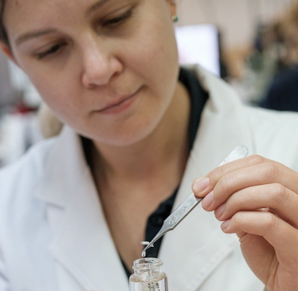 Woman in a lab coat putting a sample in a test tube with tweezers