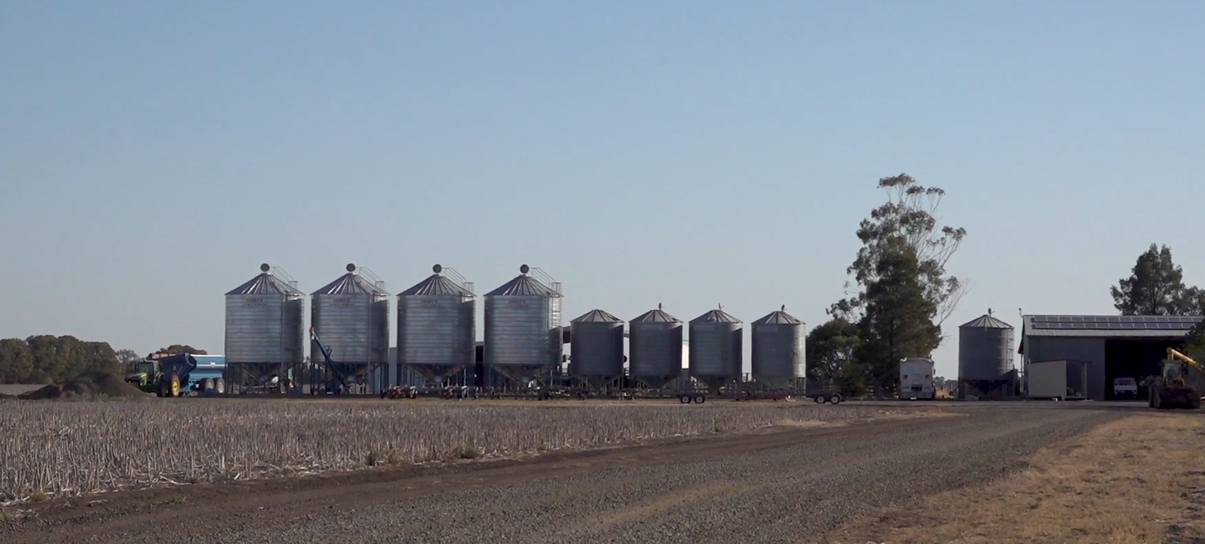 a farm with dry fields and silos in the background