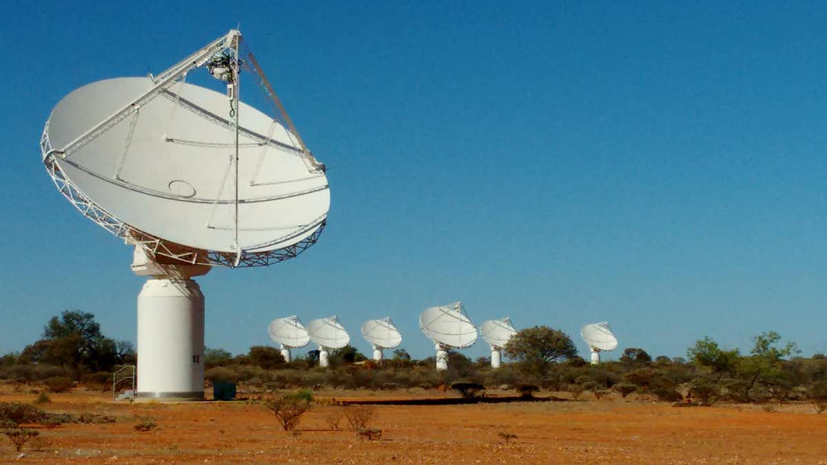 One telescope dish in the foreground and six in the background in a desert landscape