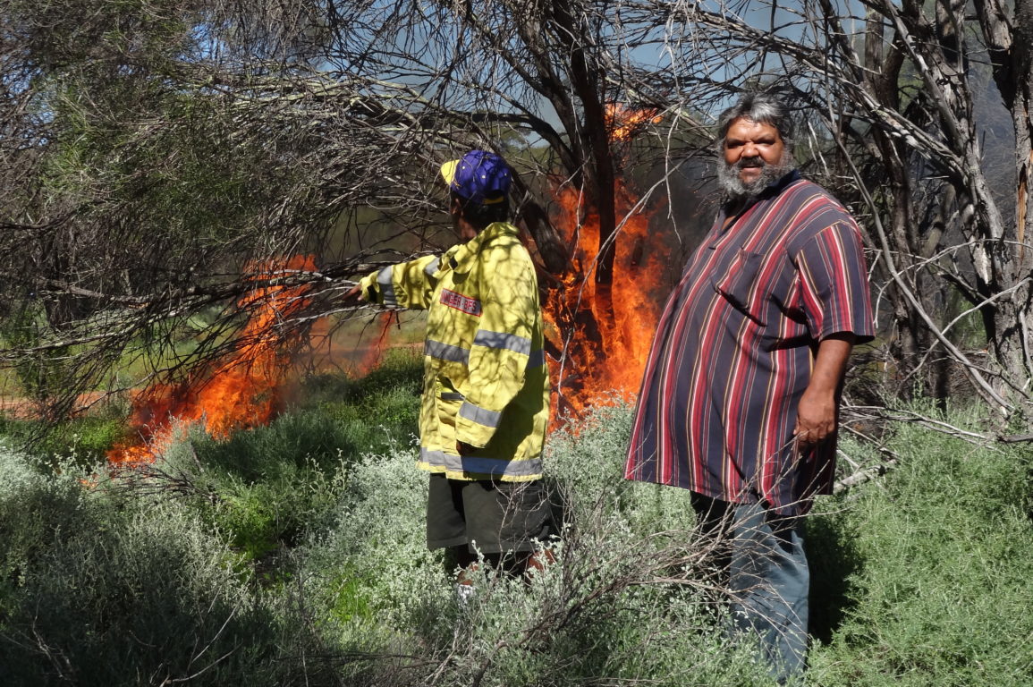 Two men light a fire in the bush