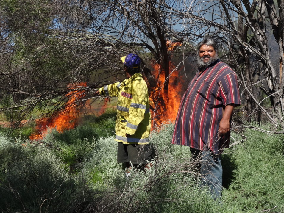 Two men light a fire in the bush