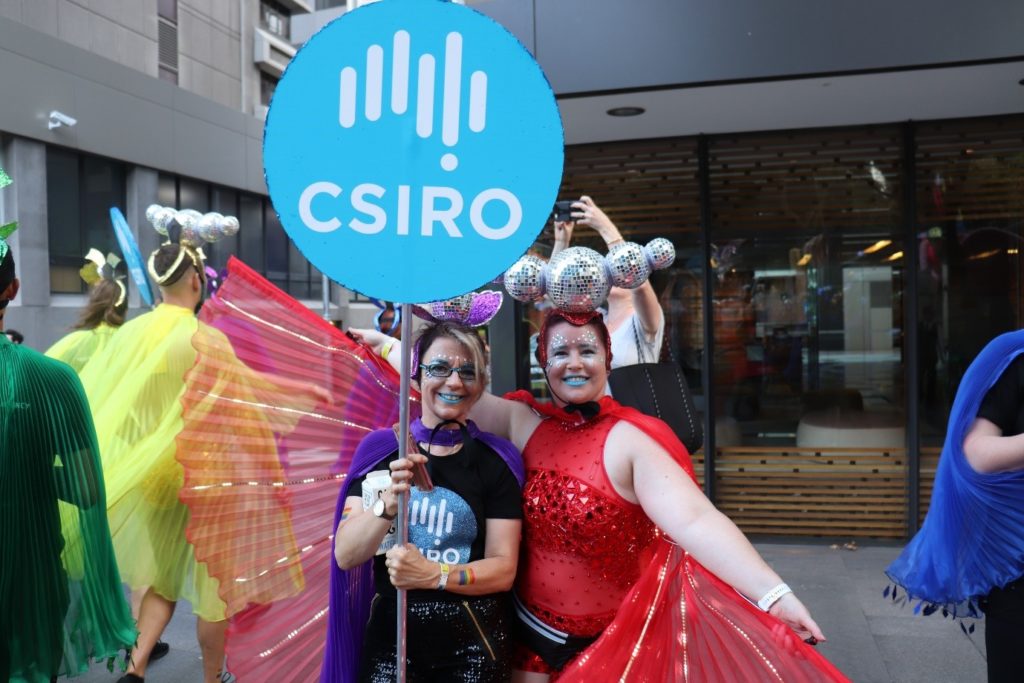 Two female staff members in glittery costumes holding up a blue csiro sign