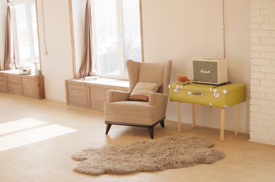 Loungeroom with armchair, sheepskin and curtains open with sun coming in window