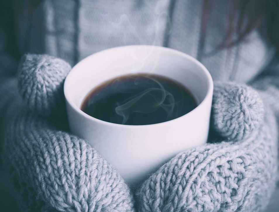 cup of coffee with two hands wearing mittens holding the cup