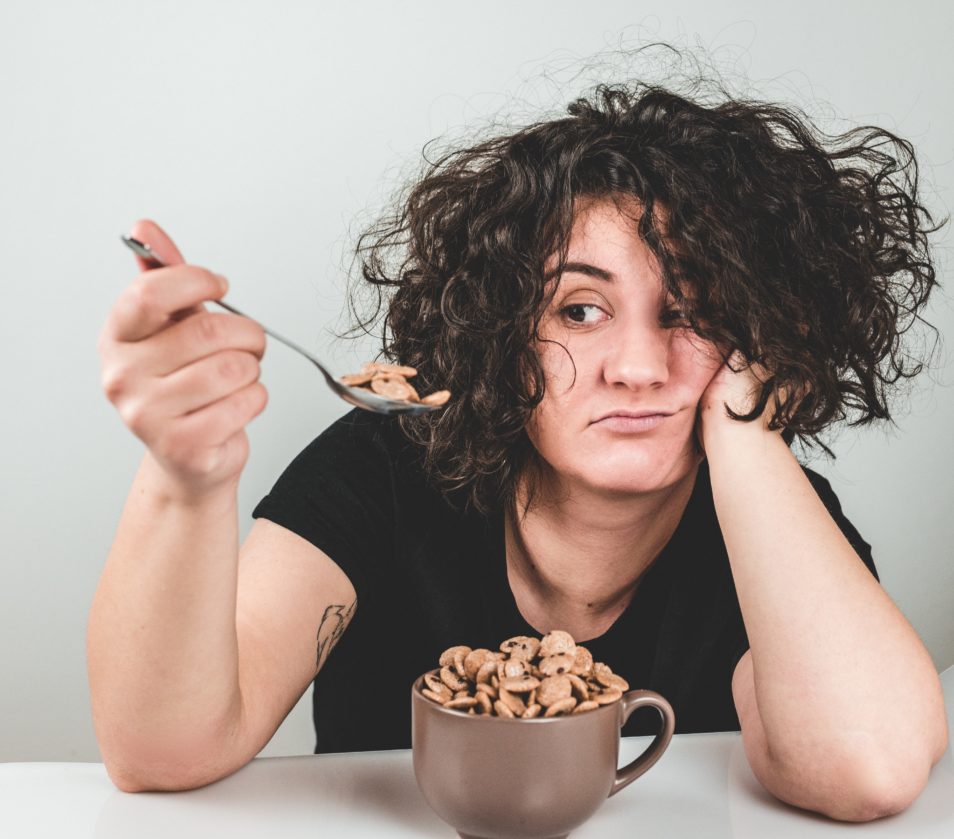 woman eating cereal out of a cup looking unhappy