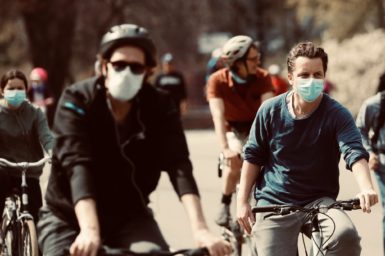 people in face masks riding bikes in town