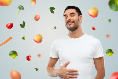 man with his hand on his gut and healthy fruit and veg around him