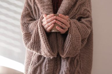 A woman wearing a wooly cardigan holding a coffee cup