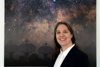 Dr Chenoa Tremblay stands in front of an image of a galaxy