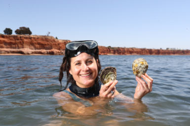 Woman in the water wearing goggles on her head, holding oysters