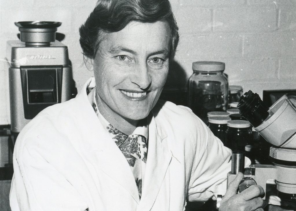 Image of a smiling woman in a lab coat surrounded by chemistry equipment. 